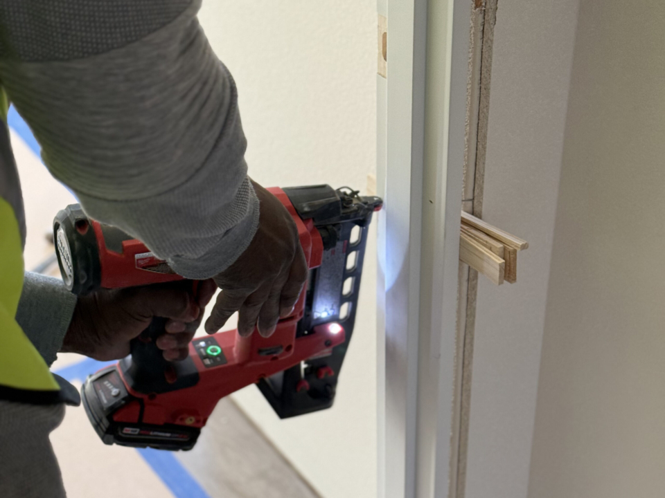 Nail gun attaching door frame to shims