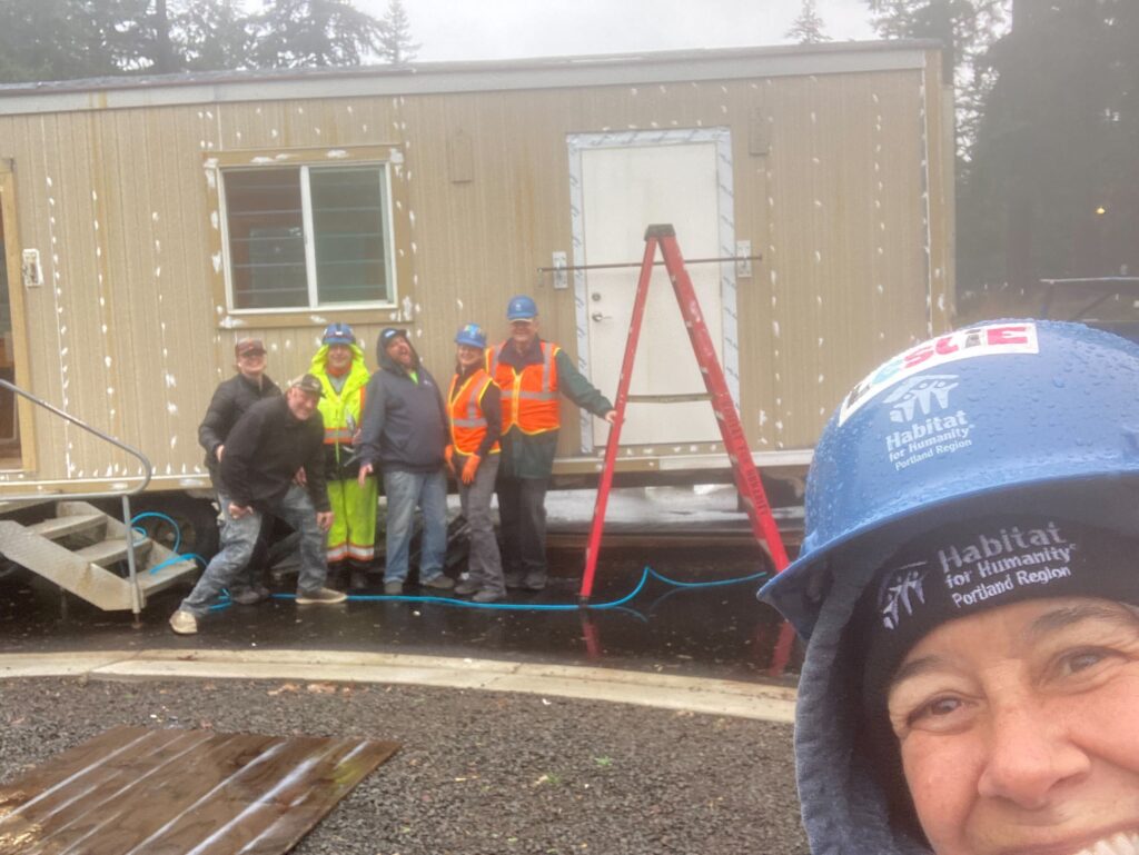 Volunteers and Habitat staff smile in front of trailer with new siding