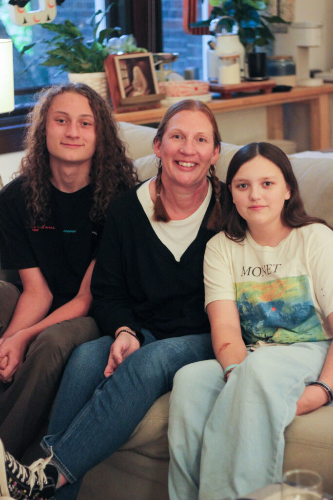 A Habitat homebuyer smiles with her two teenage children, the trio sitting on the couch in their apartment.