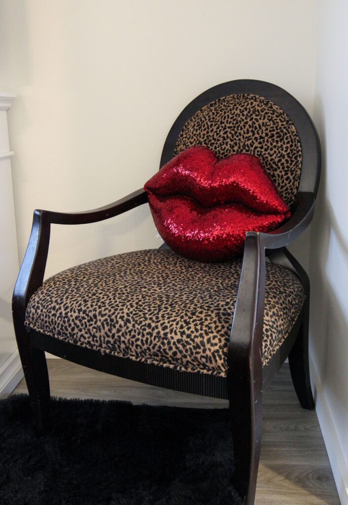 A Habitat homeowner's furniture decorates their living room. A red, lip shaped sequin pillow sits on a leopard print chair.