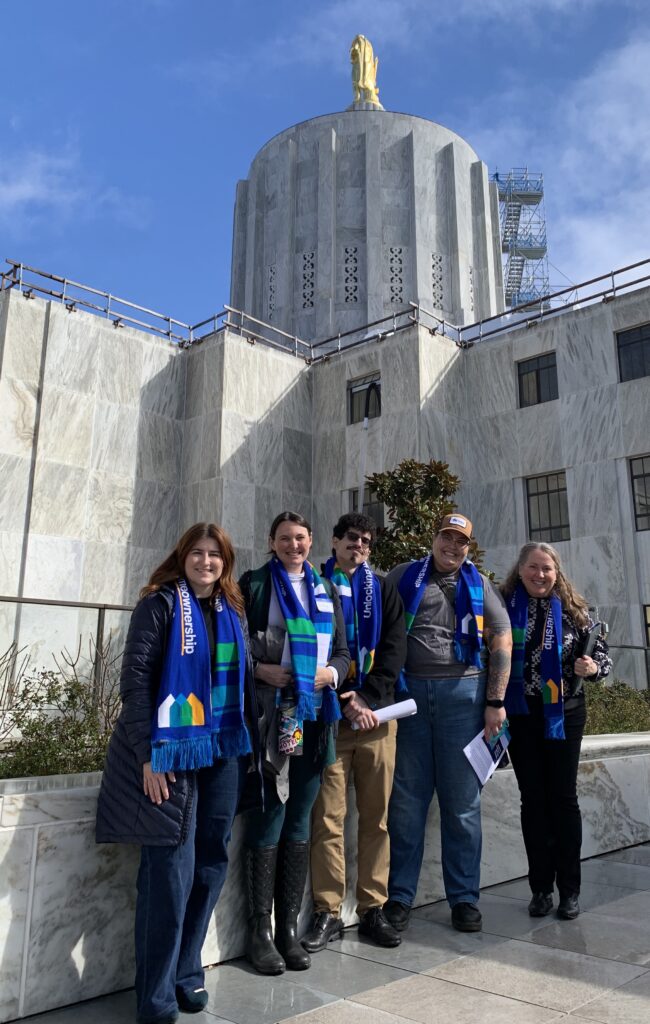 Sophia poses with four other Habitat volunteers and staff outside the Oregon State Capitol building, smiling into the camera against a background of marble and sunny blue sky.