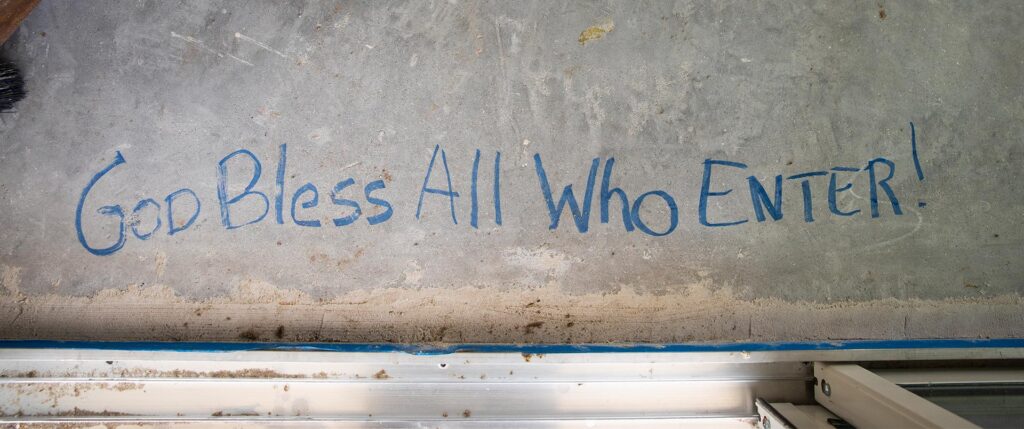 "God bless all who enter!" written in blue Sharpie on the foundation in front of the front door. 