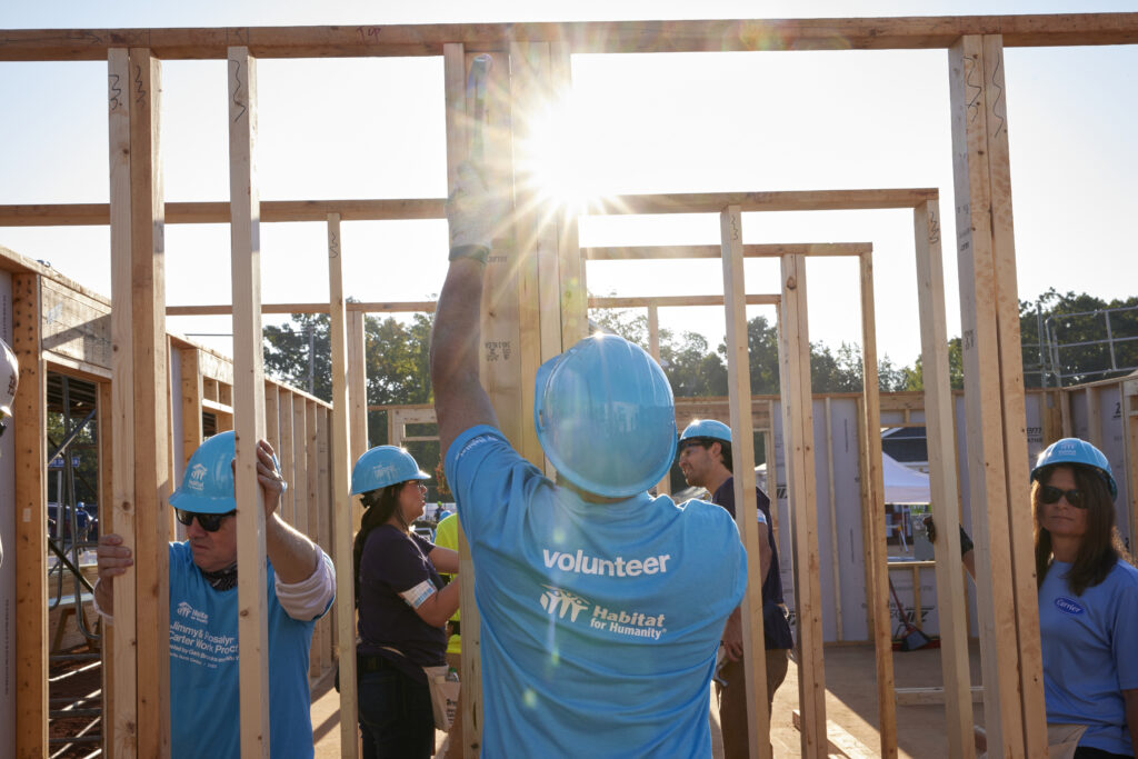  A sun ray bursts through the framing beams of a home as volunteers work to hold it steady. 
