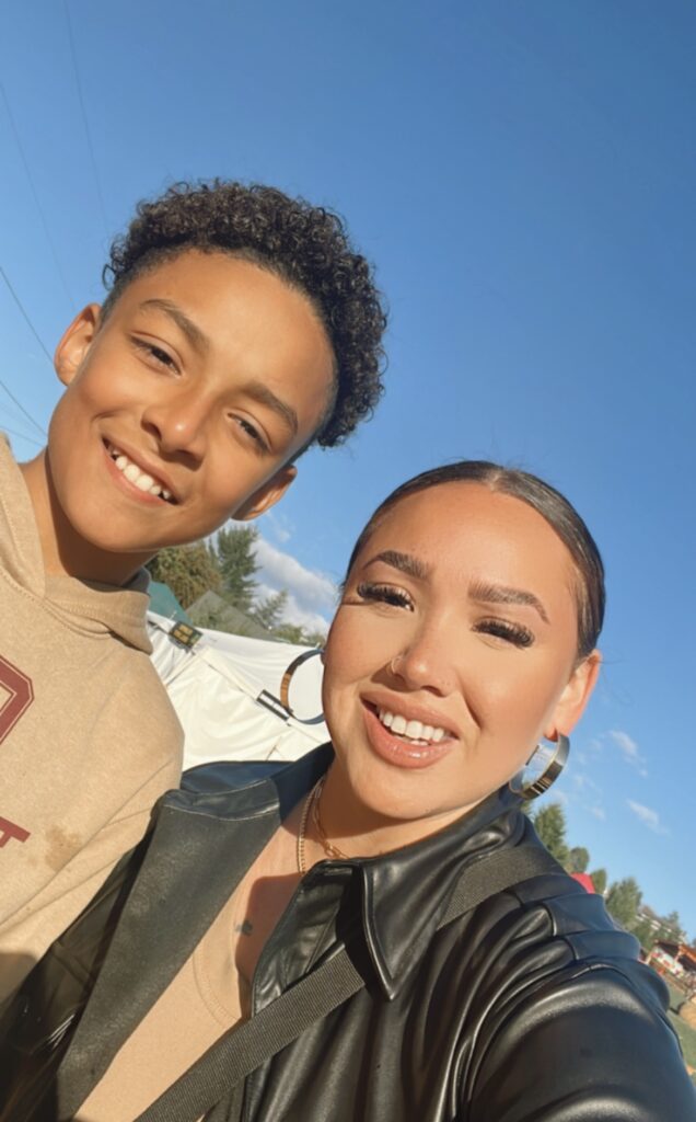 Valencia and her son Andrew smile together in a seflie, brightly lit against a clear blue sky.