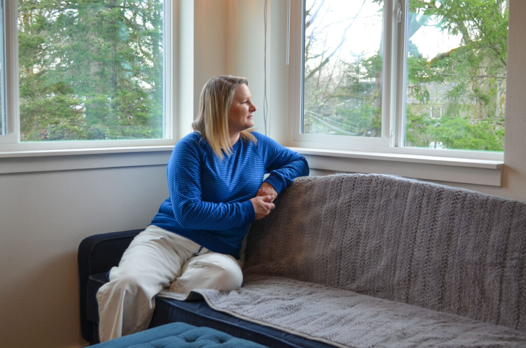 Habitat homeowner Duffy looks out the window in her new home, surrounded by a view full of greenery.