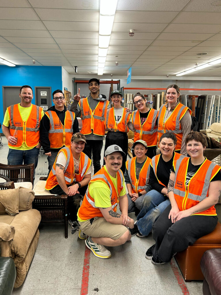 Habitat's Ambassador Council members smile, clad in high-vis vests and surrounded by furniture at a ReStore.