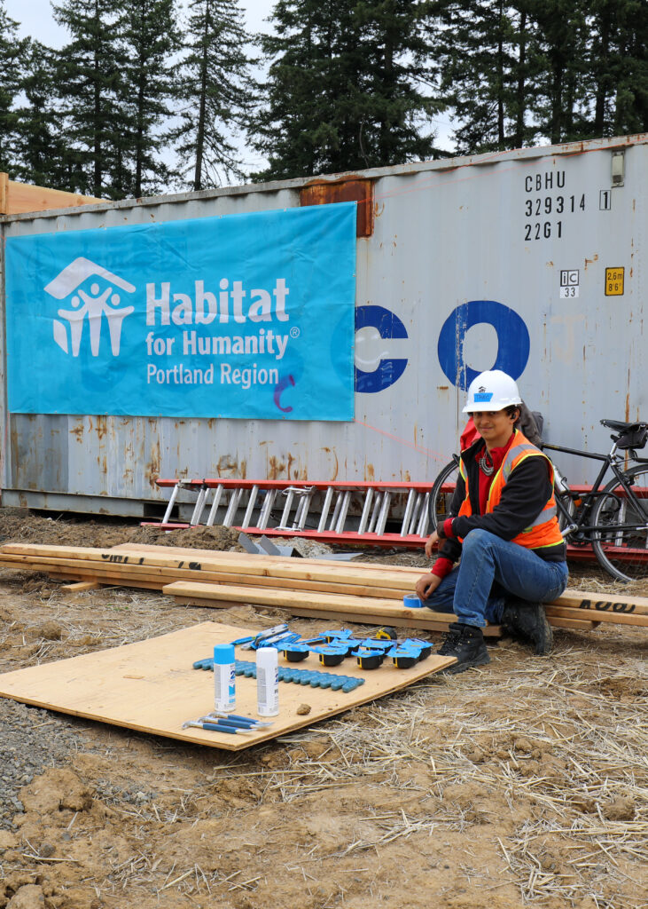 A Habitat volunteer clad in a safety vest and hard hat sits with his materials lined up.