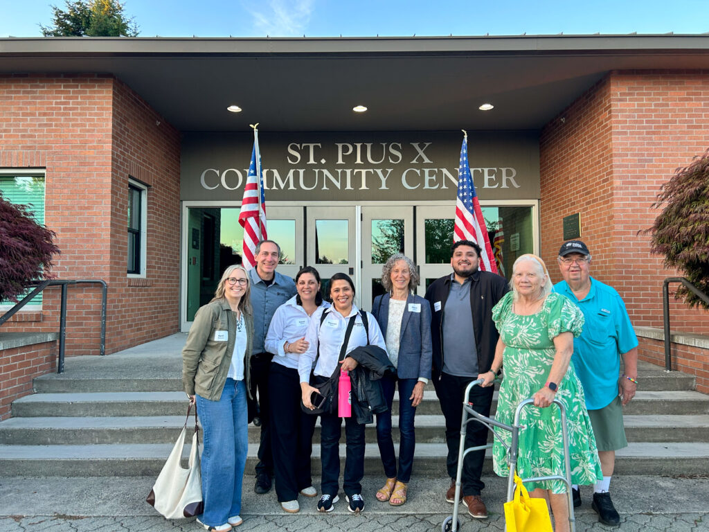 A group of Habitat supporters and staff smile warmly outside a community center.