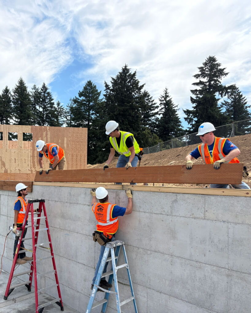 Five volunteers place a long beam atop the a building's foundation.