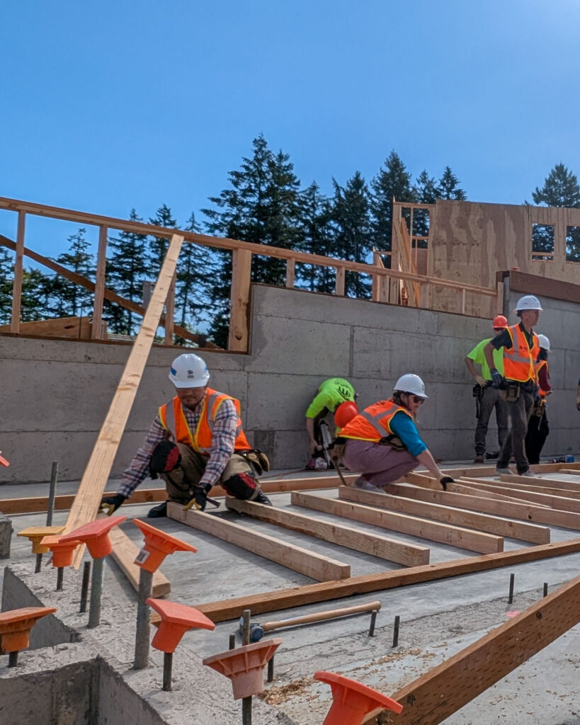 Volunteers in safety gear arrange beams for an interior wall.